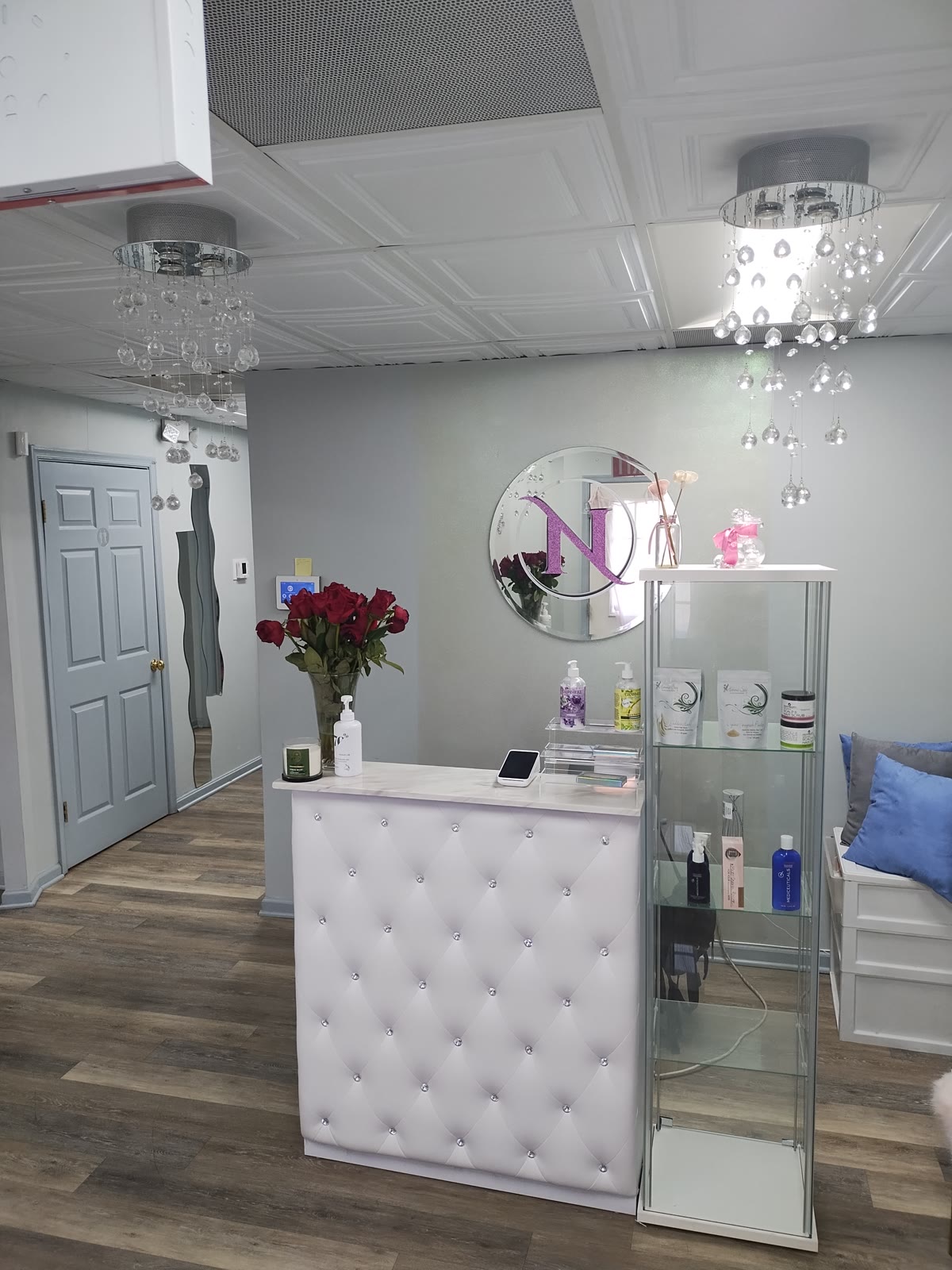 Front salon reception area with tufted display counter, product shelving, and crystal chandeliers